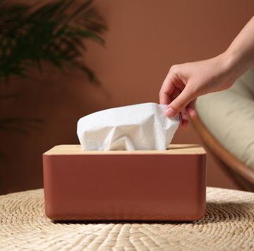 woman taking paper tissue out of box on table indoors, closeup