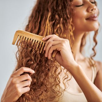 hair care, beauty and woman brushing her curly hair with a wooden comb during her self care routine beautiful, young and hispanic girl combing her clean natural locks in a studio with copy space